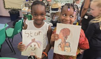 two little girls holding up their drawings