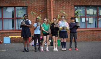 six children, standing in front of a red brick building, holding flower pots